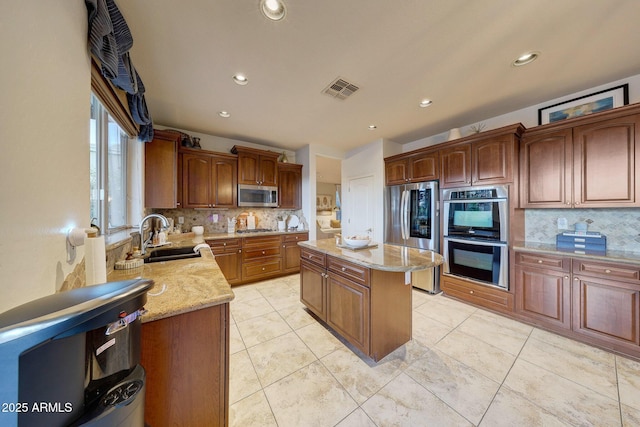 kitchen with sink, appliances with stainless steel finishes, a center island, light stone counters, and tasteful backsplash