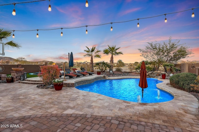 pool at dusk with a patio and pool water feature