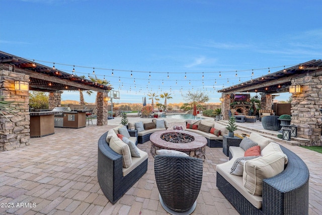 view of patio / terrace featuring grilling area, an outdoor fire pit, a stone fireplace, and exterior kitchen