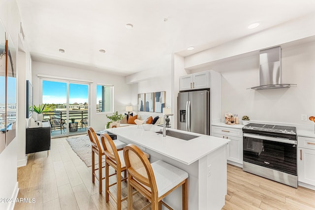 kitchen featuring white cabinetry, sink, stainless steel appliances, wall chimney range hood, and a kitchen breakfast bar