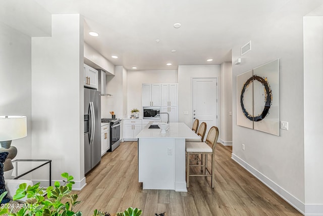 kitchen featuring a center island, appliances with stainless steel finishes, light hardwood / wood-style floors, white cabinetry, and a breakfast bar area