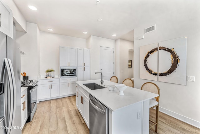 kitchen featuring stainless steel appliances, an island with sink, light hardwood / wood-style floors, a breakfast bar area, and white cabinets