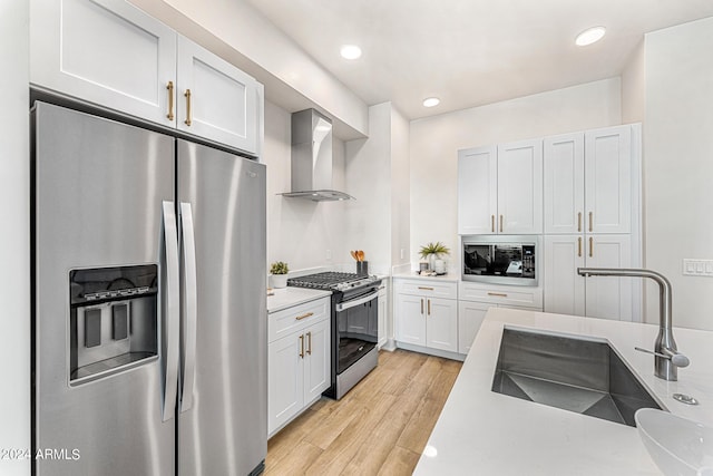 kitchen with white cabinets, wall chimney range hood, sink, appliances with stainless steel finishes, and light hardwood / wood-style floors