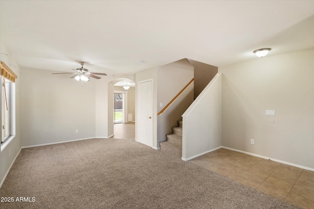 tiled spare room with baseboards, arched walkways, a ceiling fan, stairway, and carpet flooring