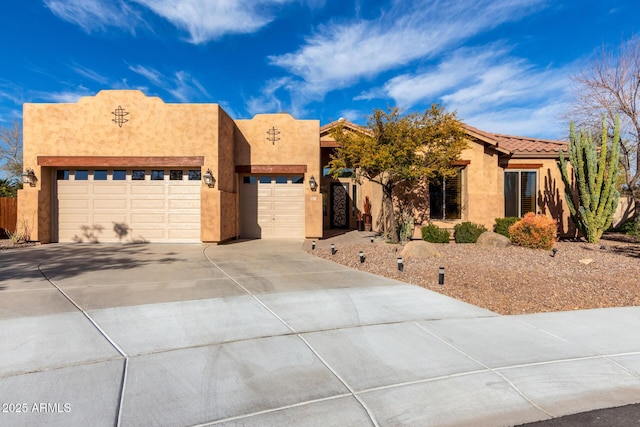 pueblo revival-style home featuring a garage, a tile roof, concrete driveway, and stucco siding