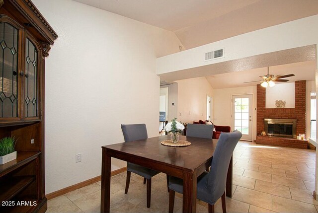 dining area featuring vaulted ceiling, a brick fireplace, light tile patterned floors, and ceiling fan