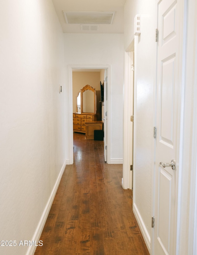 hall with visible vents, baseboards, and dark wood-style floors