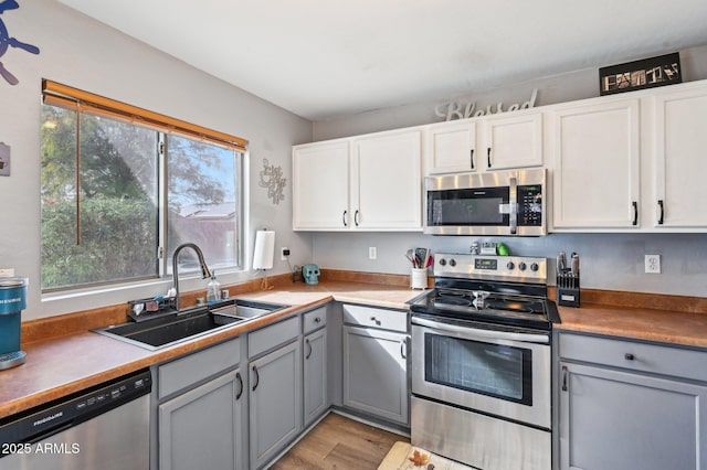 kitchen with gray cabinets, appliances with stainless steel finishes, white cabinetry, sink, and plenty of natural light