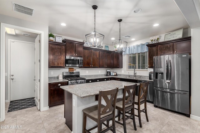 kitchen featuring visible vents, dark brown cabinets, a kitchen island, appliances with stainless steel finishes, and a sink