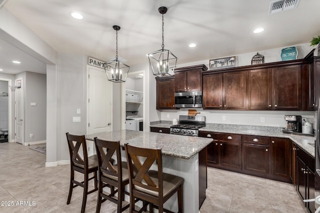 kitchen featuring washing machine and clothes dryer, visible vents, a center island, light stone counters, and stainless steel appliances