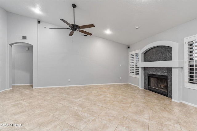 unfurnished living room with arched walkways, a tile fireplace, visible vents, a ceiling fan, and vaulted ceiling