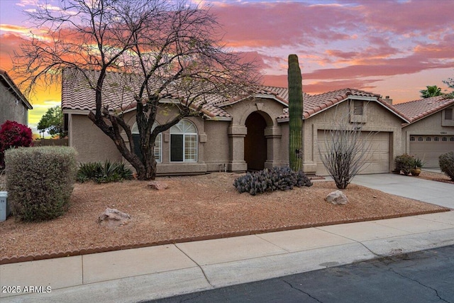 view of front facade with driveway, a tile roof, an attached garage, and stucco siding