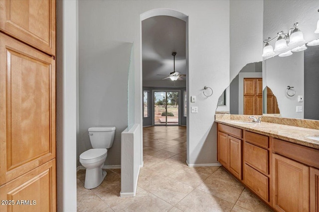 full bath featuring double vanity, toilet, ceiling fan, a sink, and baseboards