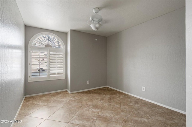 spare room featuring a textured wall, baseboards, and ceiling fan