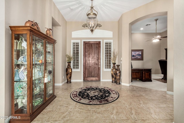 tiled foyer entrance featuring visible vents, arched walkways, baseboards, and ceiling fan with notable chandelier