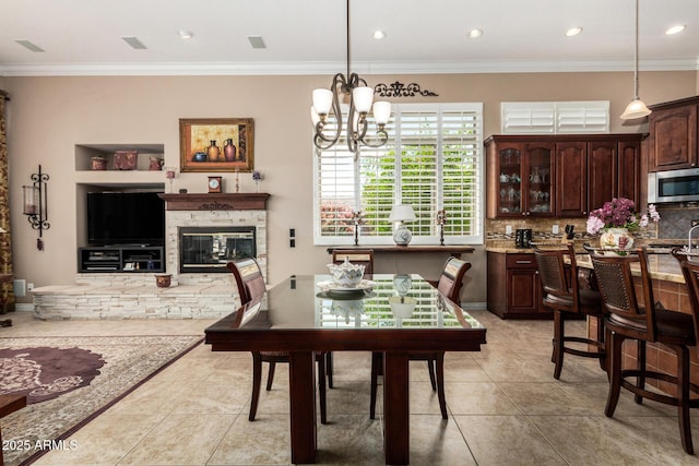 dining space featuring crown molding, an inviting chandelier, a stone fireplace, and light tile patterned floors