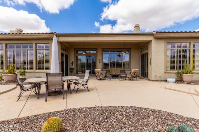back of house with ceiling fan, stucco siding, a chimney, an outdoor living space, and a patio area