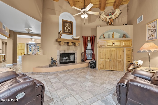 living room featuring wood ceiling, ceiling fan, beam ceiling, a towering ceiling, and a tiled fireplace