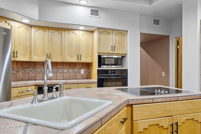 kitchen featuring tile countertops, tasteful backsplash, sink, black appliances, and light brown cabinets