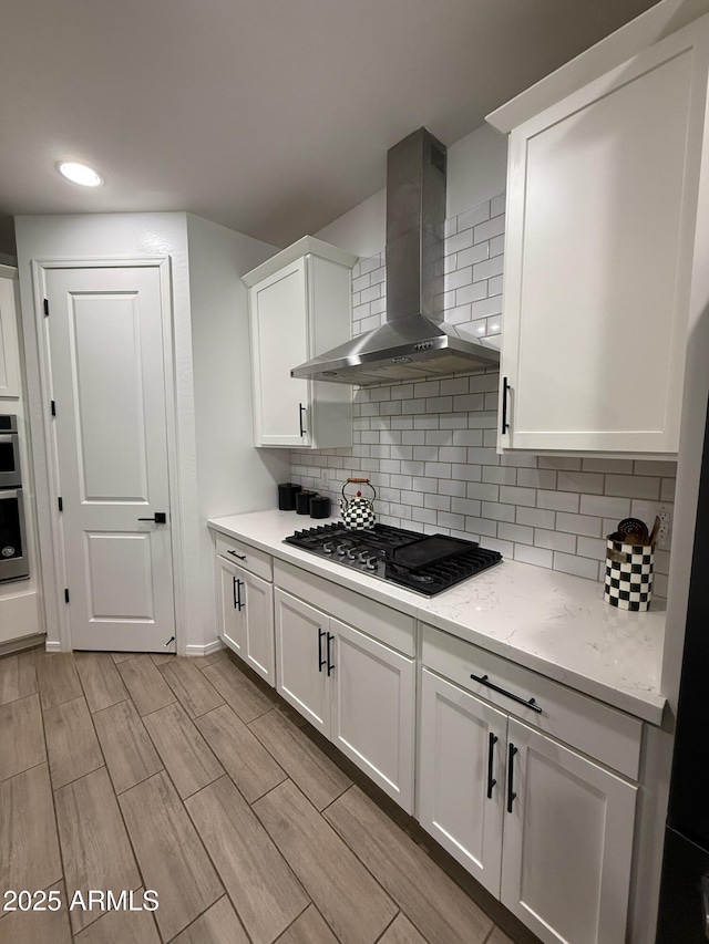 kitchen with tasteful backsplash, wall chimney range hood, black gas stovetop, and white cabinets