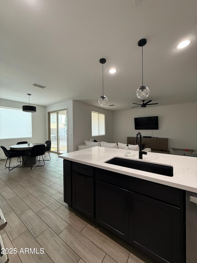 kitchen with hanging light fixtures, dishwasher, light stone countertops, and sink