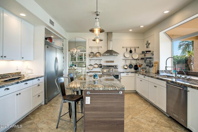 5281 W Quail Ave, Glendale, AZ 85308 - kitchen with wall chimney range hood, appliances with stainless steel finishes, a sink, dark stone counters, and a chandelier