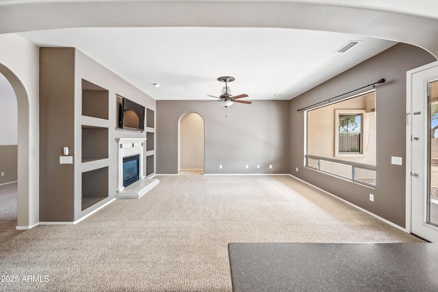 19245 W Pasadena Ave, Litchfield Park, AZ 85340 - unfurnished living room with arched walkways, built in shelves, baseboards, a ceiling fan, and a glass covered fireplace