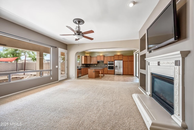19245 W Pasadena Ave, Litchfield Park, AZ 85340 - unfurnished living room with ceiling fan, light carpet, arched walkways, a glass covered fireplace, and baseboards