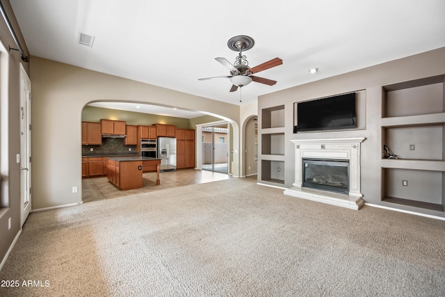 19245 W Pasadena Ave, Litchfield Park, AZ 85340 - unfurnished living room with arched walkways, a ceiling fan, light carpet, built in features, and a glass covered fireplace