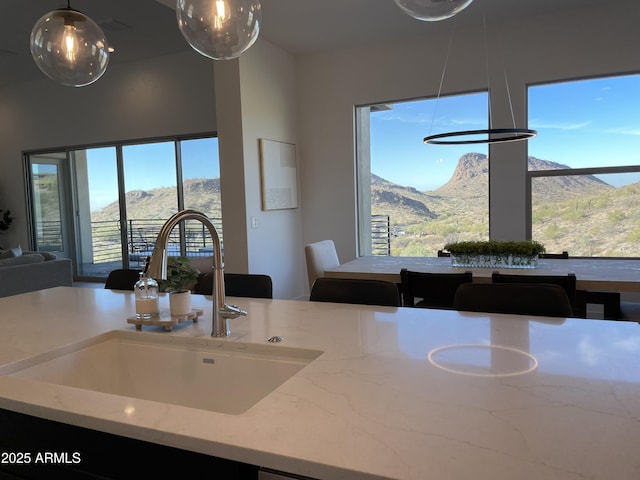 kitchen with hanging light fixtures, a mountain view, sink, and light stone countertops