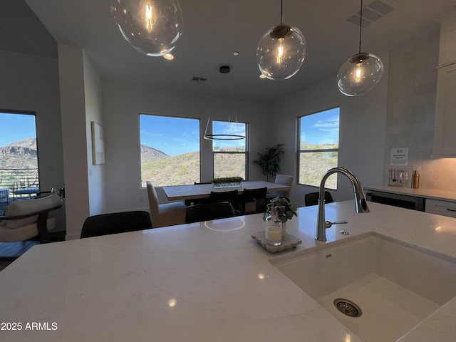 kitchen featuring a mountain view, sink, light stone countertops, and hanging light fixtures