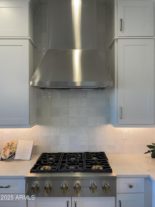 kitchen featuring decorative backsplash, light stone counters, stainless steel gas stovetop, and wall chimney range hood