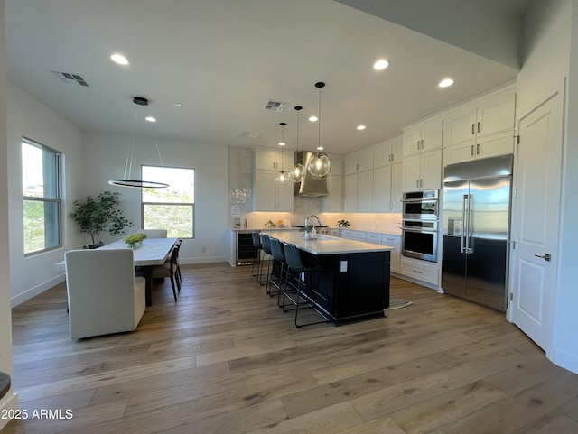 kitchen with a center island with sink, white cabinetry, hanging light fixtures, and appliances with stainless steel finishes