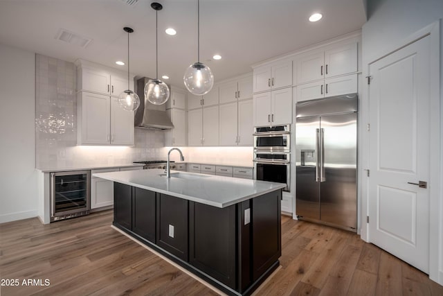 kitchen featuring stainless steel appliances, beverage cooler, a kitchen island with sink, sink, and pendant lighting