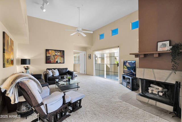 living room featuring a tiled fireplace, a towering ceiling, light colored carpet, and ceiling fan