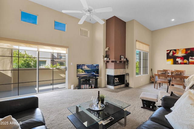 living room featuring light carpet, a tile fireplace, ceiling fan, and a high ceiling