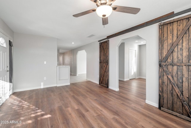 unfurnished living room with ceiling fan, a barn door, and hardwood / wood-style floors