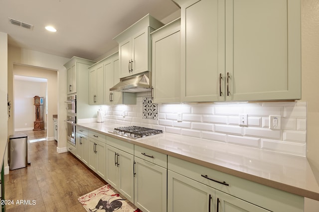 kitchen with decorative backsplash, light stone counters, stainless steel appliances, and light hardwood / wood-style floors