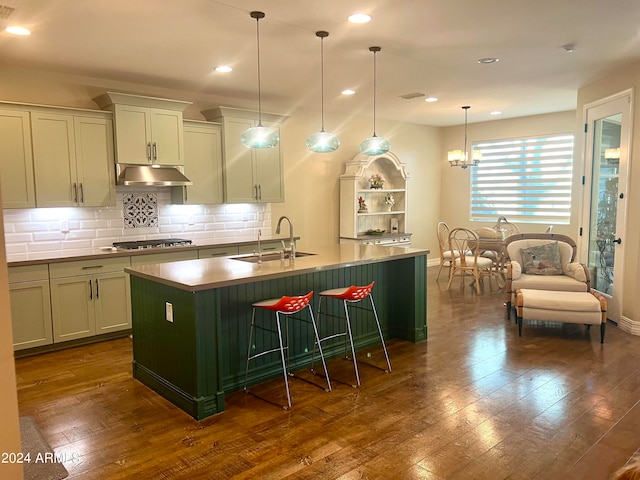 kitchen featuring sink, hanging light fixtures, dark wood-type flooring, decorative backsplash, and a center island with sink