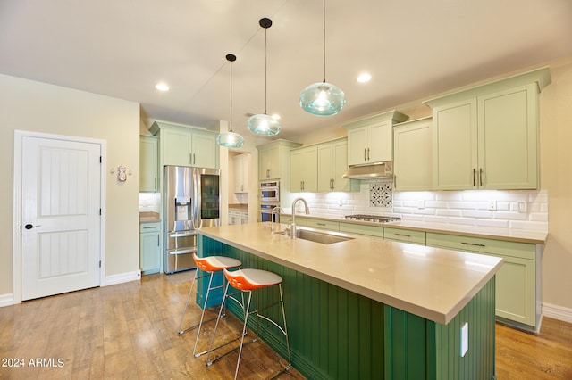 kitchen with light hardwood / wood-style floors, sink, stainless steel appliances, and an island with sink