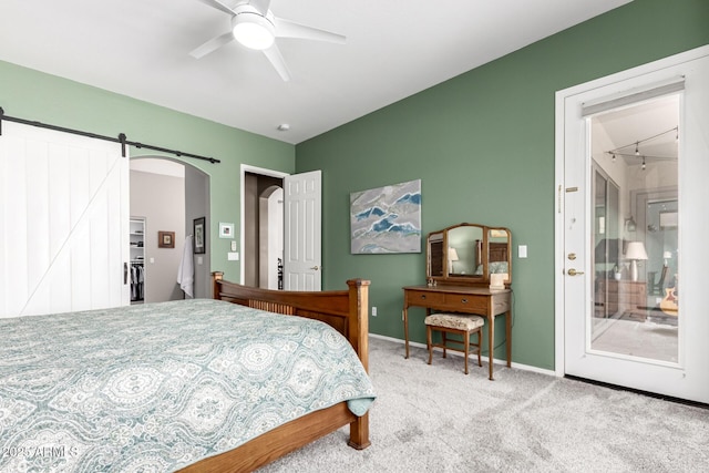 carpeted bedroom featuring a barn door, a ceiling fan, and baseboards