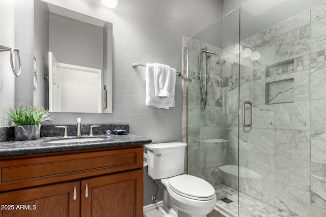 bathroom featuring a stall shower, a textured wall, vanity, and toilet
