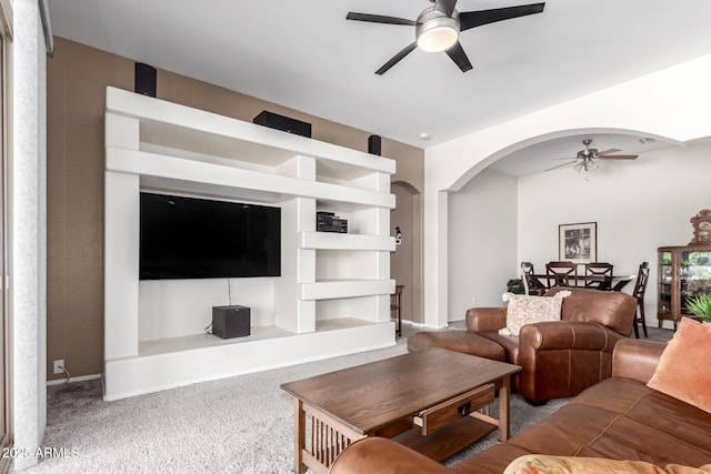 carpeted living area featuring ceiling fan and arched walkways