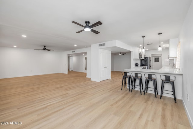 kitchen featuring light hardwood / wood-style floors, pendant lighting, kitchen peninsula, white cabinetry, and stainless steel fridge