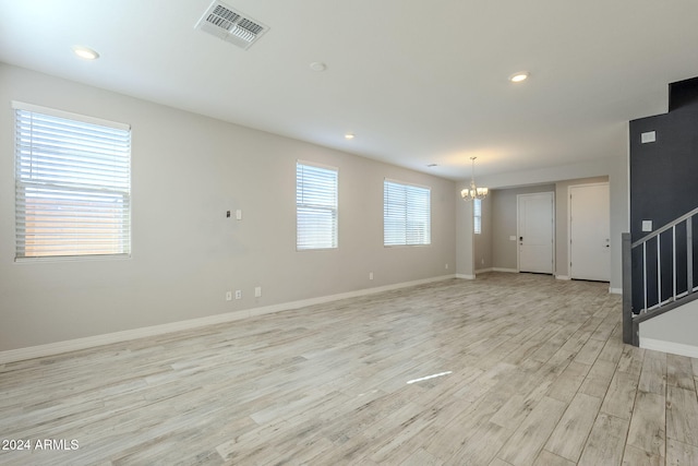 empty room featuring plenty of natural light, light hardwood / wood-style floors, and an inviting chandelier