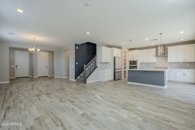 kitchen with a center island with sink, wall chimney exhaust hood, hanging light fixtures, and light hardwood / wood-style flooring