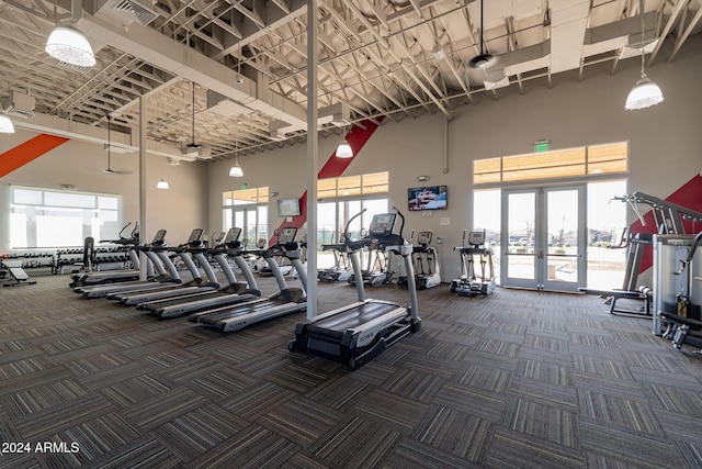 gym featuring dark carpet, a towering ceiling, a healthy amount of sunlight, and french doors