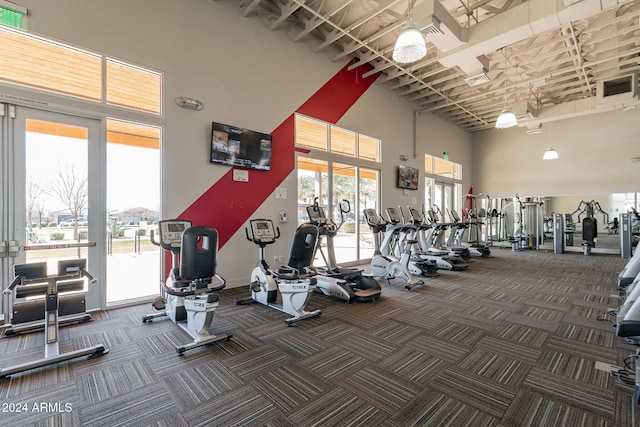 exercise room with a healthy amount of sunlight, a high ceiling, and dark colored carpet