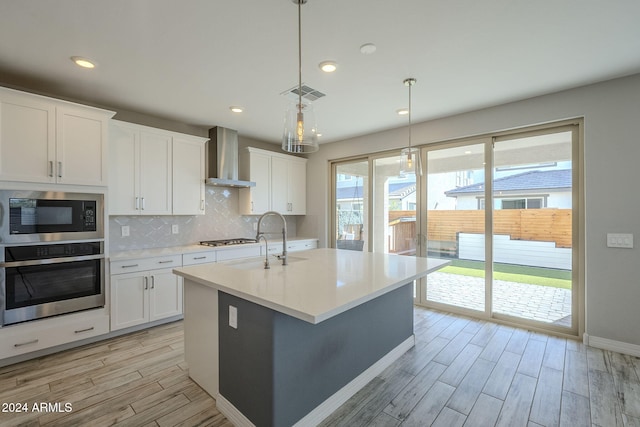 kitchen featuring white cabinets, appliances with stainless steel finishes, decorative light fixtures, and wall chimney range hood