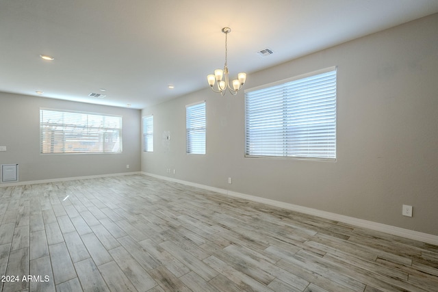 spare room featuring light wood-type flooring and a chandelier